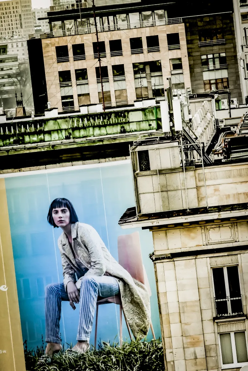 Seated billboard figure above worn city rooftops